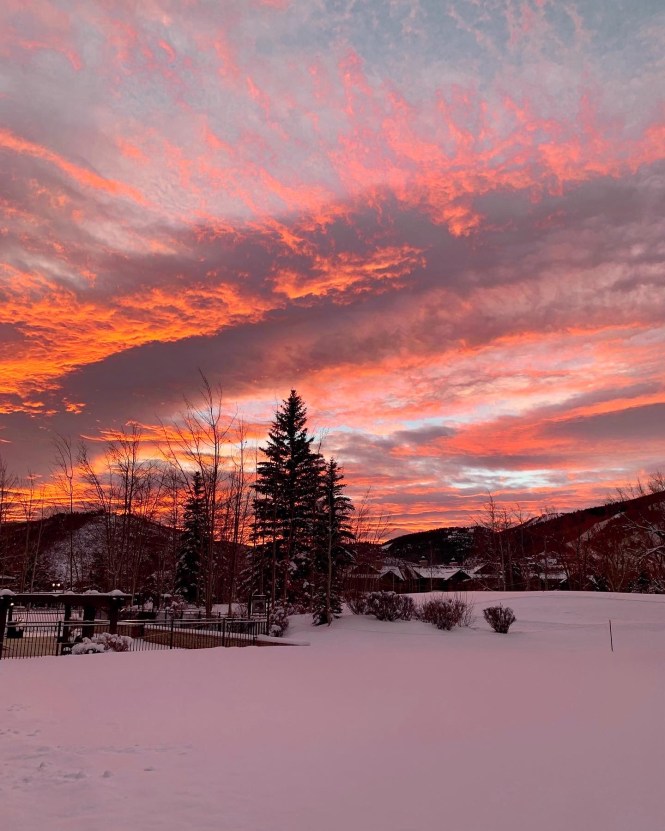 early morning winter sunrise with pink and orange sky in the snowy mountains of park city, utah