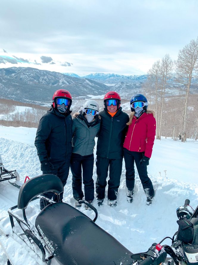 four friends standing together in ski gear in the snow of the utah mountains with the rocky mountains in the background