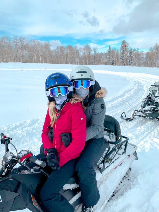 two friends on a snowmobile with blonde hair and ski gear in the snow